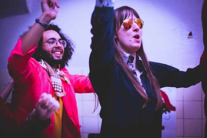 A man and a woman dance and raise their arms at a Disco Elysium LARP.