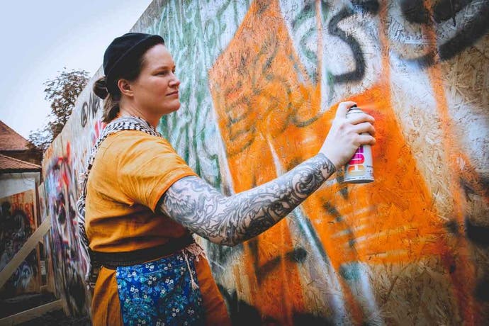 A woman spray-paints a graffiti wall at a Disco Elysium LARP.