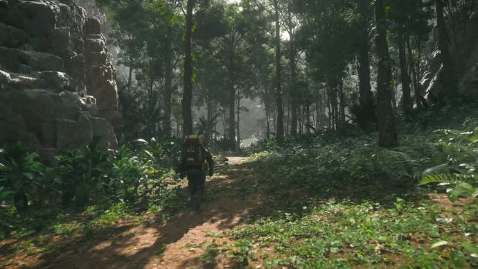 Death Stranding 2 trailer screenshot showing Sam Bridges carrying a package on his back through a lush green forest