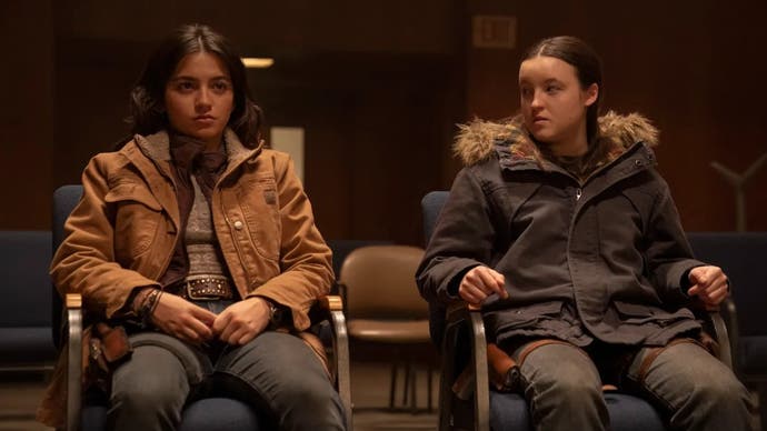 Dina and Ellie in the second season of TLOU. They are sitting on chairs in cosy jackets. Ellie is looking at Dina, who is looking towards the camera as though towards someone off screen