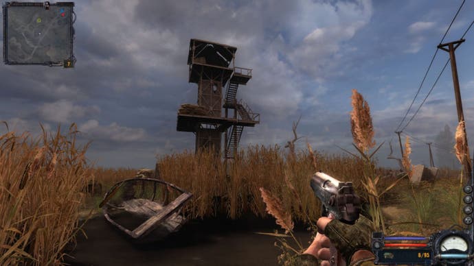 The player crouches in the marshy reeds near a boat and observation tower in Stalker: Clear Sky.