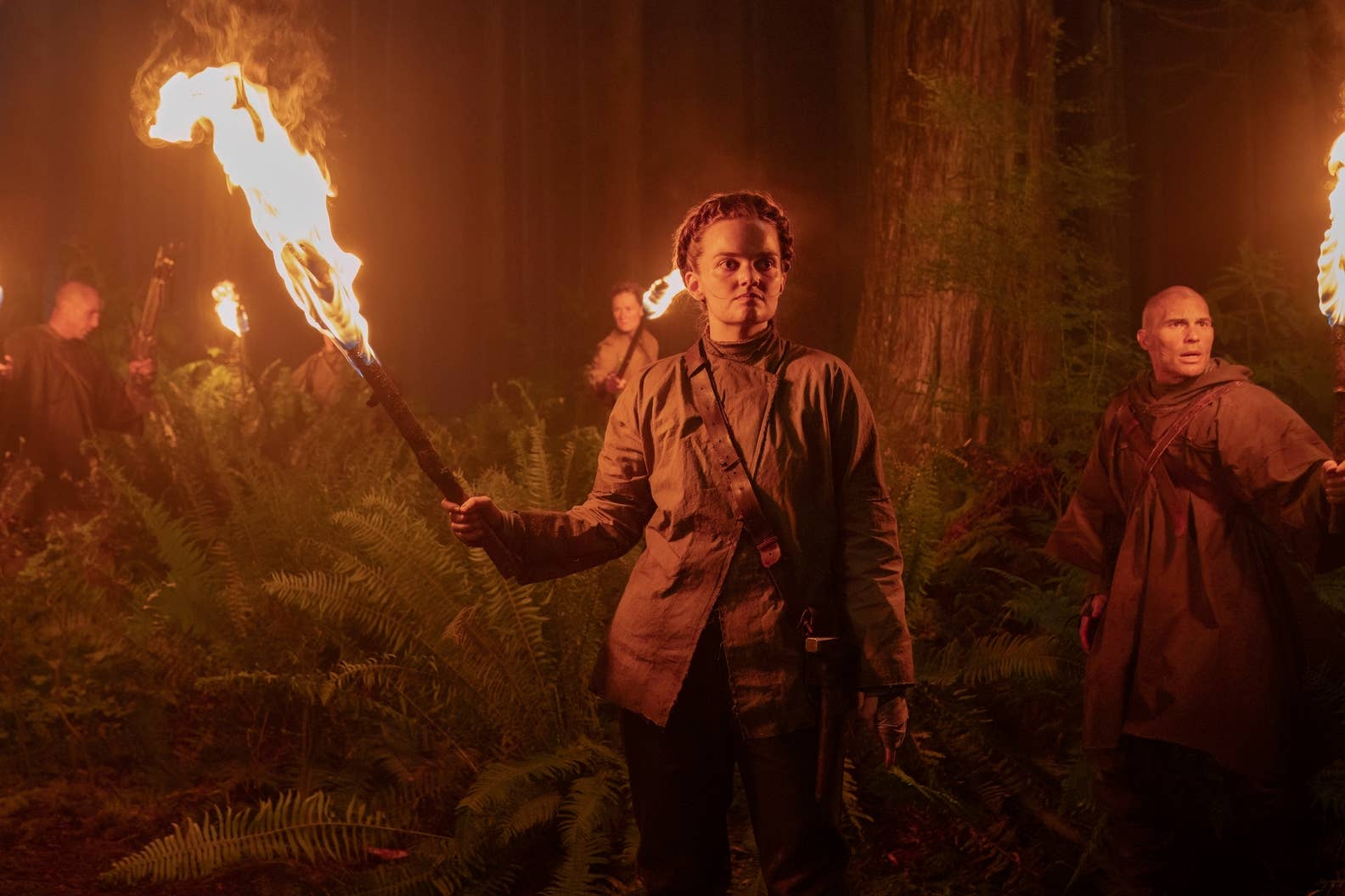 Members of the Scars hold up torches in a wooded area in TLOU season two