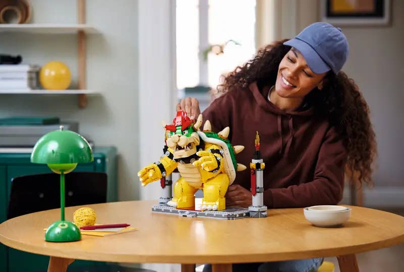 A large Lego Bowser set on a table, with a smiling person sat behind it. They look delighted with their afternoon's work.